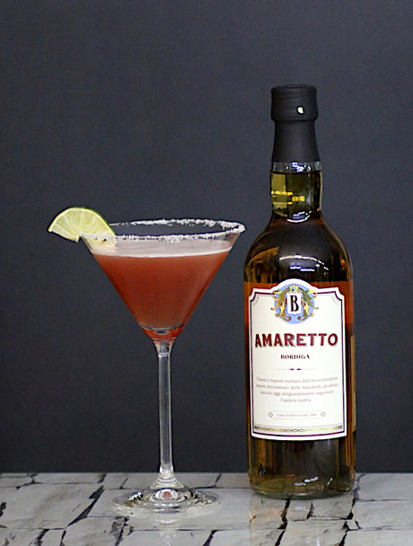 Amaretto Cranberry Kiss Cocktail im Martini-Glas mit Limette neben Amaretto Bordiga Flasche