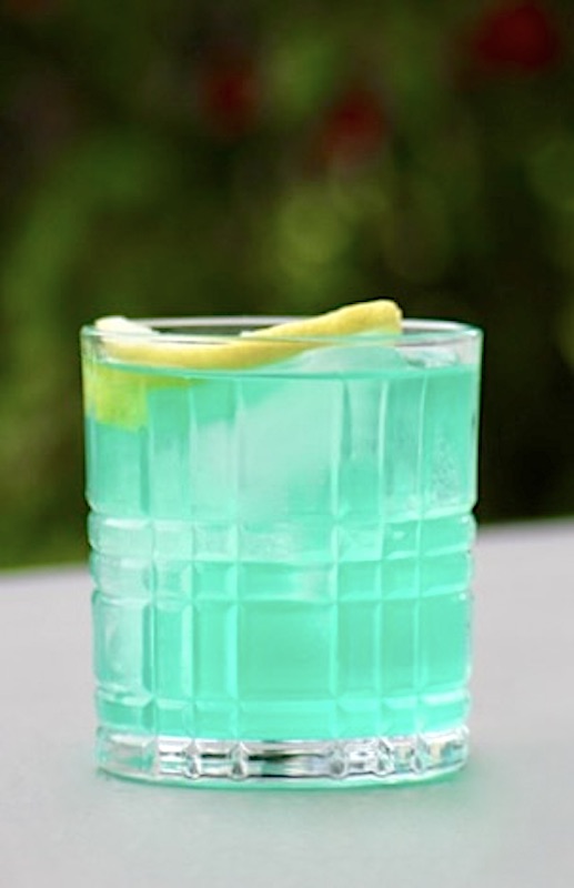 "Ein erfrischender Blue Lagoon Twist Cocktail in einem Whisky-Glas, serviert mit Eiswürfeln und einer Zitronenscheibe als Garnitur. Der Cocktail hat eine leuchtend blaue Farbe und vermittelt tropisches Flair.