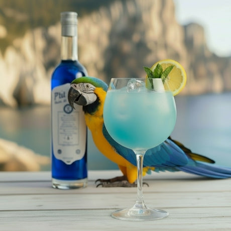 L’Ara Qui Rit Cocktail im Spritzglas mit Zitrone und Minze, daneben Pastis P’tit Bleu Flasche und Ara-Papagei.