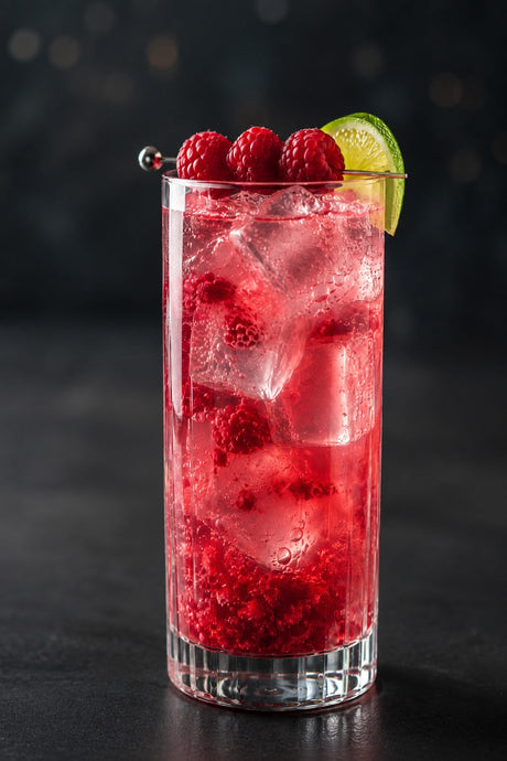 Raspberry Collins Cocktail im Collins-Glas mit Eis, Himbeeren und Limettenscheibe vor dunklem Hintergrund