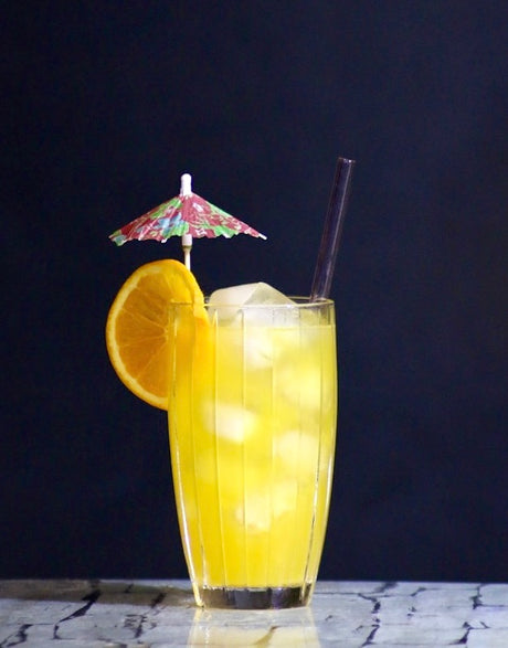 Sunshine Radiance Cocktail mit Orangenscheibe und Schirmchen vor dunklem Hintergrund
