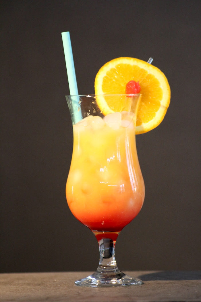 Alkoholfreier Tequila Sunrise im Glas, dekoriert mit Orangenscheibe und Kirsche, auf Eis serviert, mit Strohhalm.