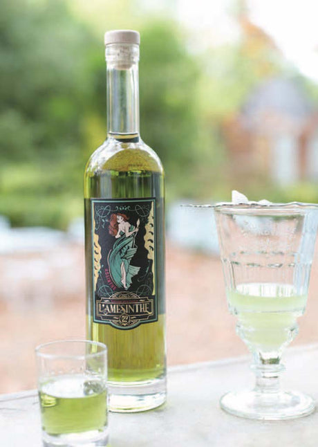 L'Amesinthe Absinthflasche und grüner Absinth im Glas mit Zucker, im Freien auf einem Tisch platziert.