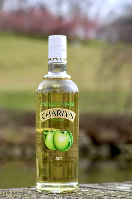 Flasche Charly's Manzana Verde, alkoholfreies Getränk mit 35 % Apfelsaft, stehend auf Holz vor einem unscharfen, natürlichen Hintergrund. 