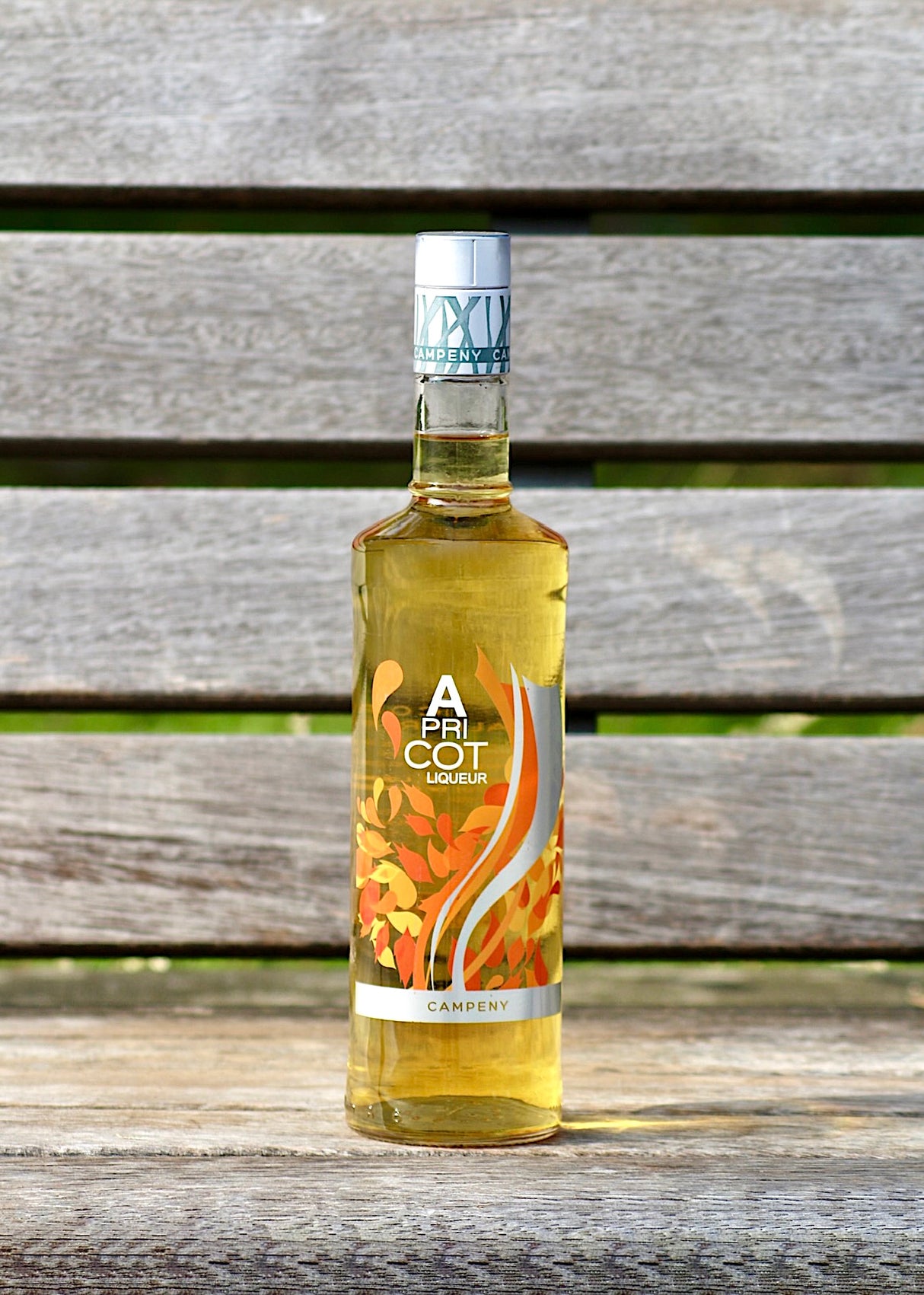 Flasche Apricot Likör von Campeny mit goldenem Inhalt auf einer Holzbank.