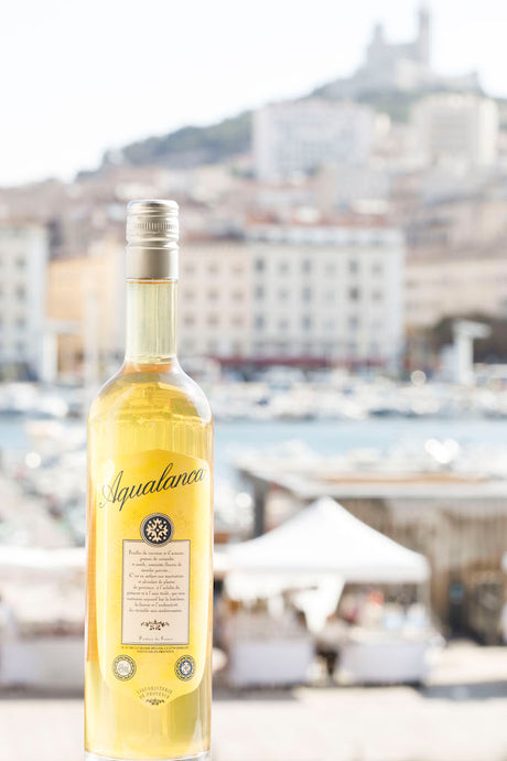 Flasche Aqualanca L'Anis d'Antan vor einem unscharfen Stadt- und Hafenhintergrund