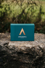 Geschlossene Arduenna Geschenkbox in Türkis mit goldenem Logo auf Naturstein vor unscharfem Grün.