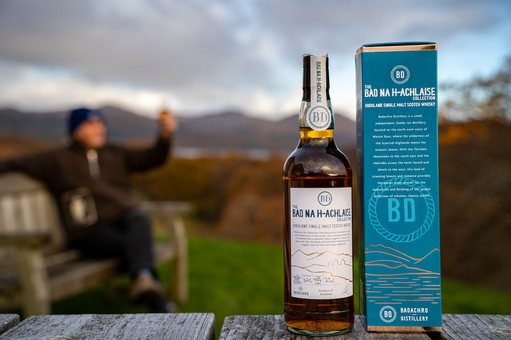 Flasche Bad na h-Achlaise Tuscan Oak Highland Single Malt Scotch Whisky mit Geschenkbox, im Hintergrund eine malerische Landschaft.