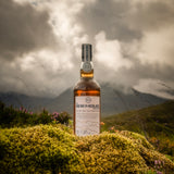 Flasche Bad na h-Achlaise Tuscan Oak Highland Single Malt Scotch Whisky auf einer grünen Mooslandschaft, im Hintergrund schottische Berge.