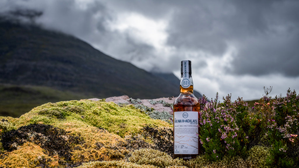 Flasche Bad na h-Achlaise Tuscan Oak Highland Single Malt Scotch Whisky auf moosbewachsenem Felsen, im Hintergrund neblige schottische Berge.