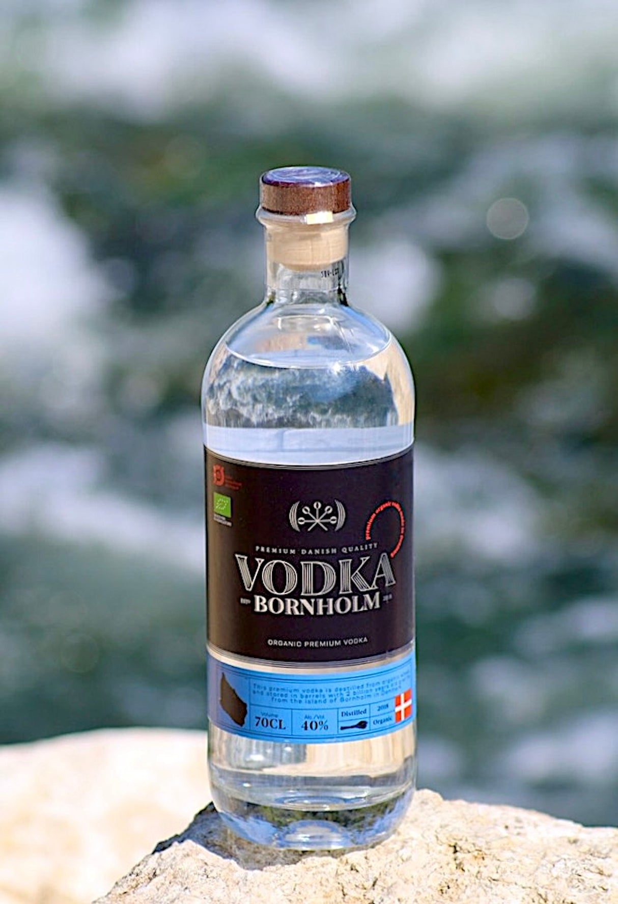 Eine Flasche Bio-Vodka Bornholm steht auf einem Felsen vor einem klaren Wasserhintergrund, der die Reinheit und Natürlichkeit des Produkts betont.