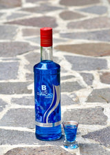 Flasche Campeny Blue Curaçao Likör neben einem kleinen Glas mit blauem Likör, platziert auf einer gepflasterten Steinfläche.