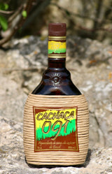 Flasche Cachaça 091 steht auf Felsen im Freien, präsentiert in einer dekorativen, mit Seil umwickelten Flasche, die in der Sonne schimmert und von natürlichem Stein umgeben ist.