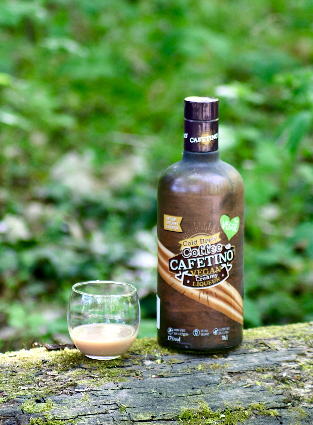 Cafetino Vegan Likör Flasche mit Glas auf moosigem Baumstamm vor grünem Naturhintergrund