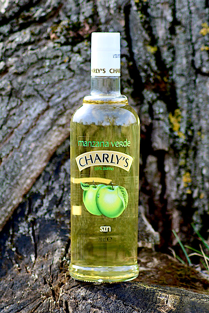 Flasche Charly's Manzana Verde, alkoholfreies Getränk mit 35 % Apfelsaft, stehend vor einer Baumrinde, mit grünem Apfelmotiv auf dem Etikett.