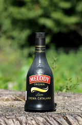Melody Crema Catalana Likör Flasche auf Baumrinde vor grünem Hintergrund