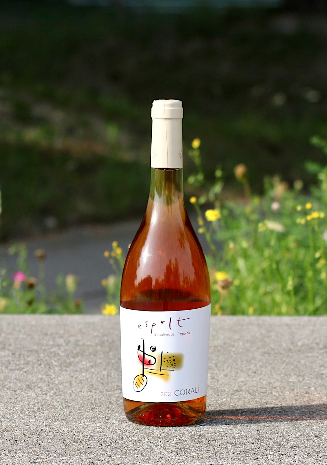 Flasche Espelt Corali Bio Rosé Wein, DO Empordà, vor einem unscharfen, blühenden Hintergrund.