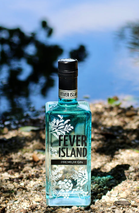 Fever Island Premium Gin Flasche am Seeufer mit blauem Wasser im Hintergrund
