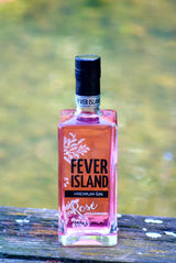 Fever Island Rose Gin Rosé Strawberry aus Mallorca in rosafarbener Flasche auf Holzbank vor grünem Hintergrund