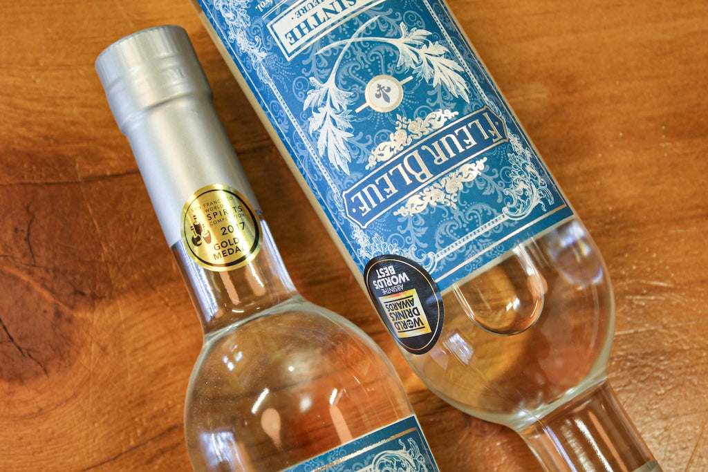 Zwei Fleur Bleue Absinth Flaschen mit blauem Etikett und Medaillen auf Holztisch