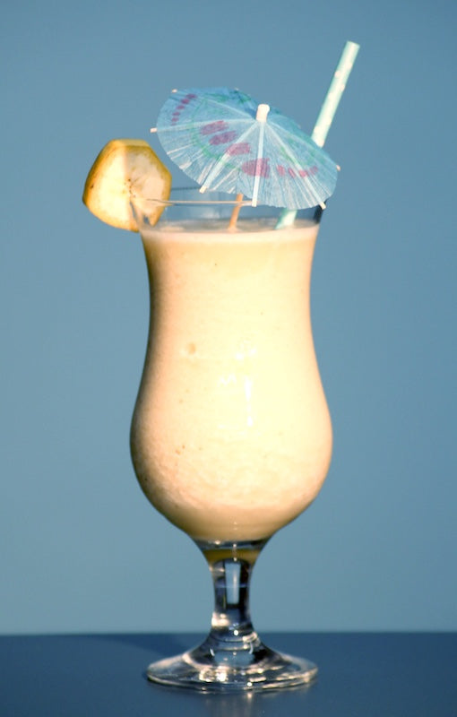 Frozen Banana Daiquiri Cocktail im Hurricane-Glas mit Strohhalm, Bananenscheibe und Schirmchen vor hellem Hintergrund
