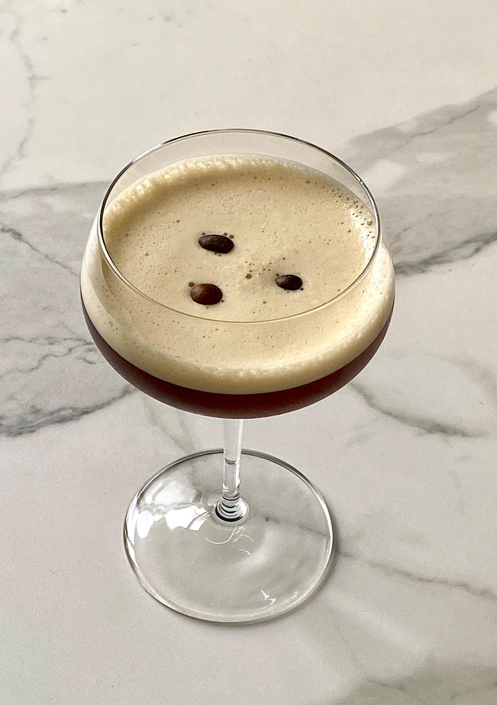 Grappa Espresso Martini in einer Coupette, von oben fotografiert, mit heller Schaumkrone und drei Kaffeebohnen.