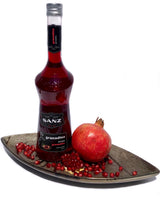 Flasche Sanz Grenadinesirup auf einer Schale mit Granatapfelkernen und einem ganzen Granatapfel