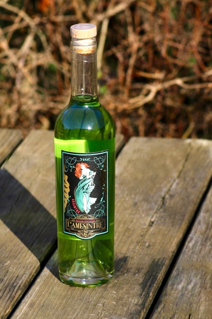 L'Amesinthe Absinthflasche auf einem Holztisch mit unscharfem Hintergrund.