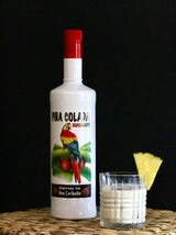Guacamayo Piña Colada Flasche mit einem Glas des cremigen Piña-Colada-Drinks und Ananasstück als Deko.
