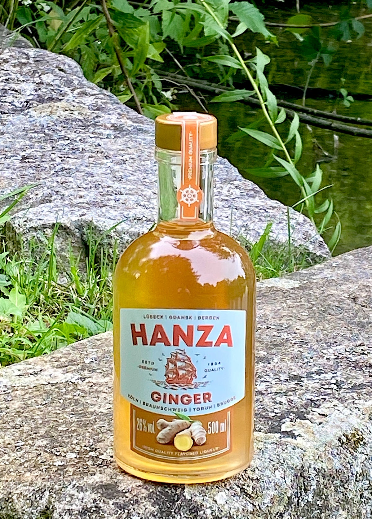 Hanza Ginger Ingwerlikör auf einem Felsen am See, Flasche mit Ingwermotiv und Segelschiff auf dem Etikett.
