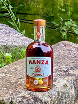 Hanza Quince Quittenlikör auf einem Felsen am See, Flasche mit Quittenmotiv und Segelschiff auf dem Etikett.
