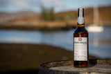 Flasche Bad na h-Achlaise Tuscan Oak Cask Strength Highland Single Malt Scotch Whisky auf einem Fass, im Hintergrund ein See mit Boot.