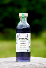 Lavendellikör Liquoristerie de Provence Flasche auf hellem Holztisch vor grünem Hintergrund