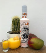 Flasche Sombrero Mexicano Mango Cream Likör mit Tequila neben einem Kaktus, Mango und gefülltem Shotglas sowie Glas mit Eis.