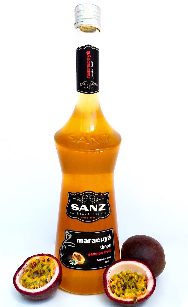 Flasche Sanz Maracuyá Sirup 70cl mit schwarzem Etikett „maracuyá sirope passion fruit“, umgeben von halben und ganzen Passionsfrüchten.