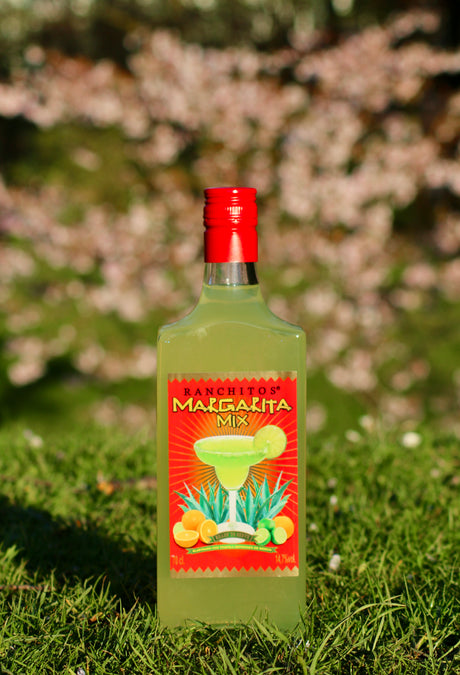 Flasche Ranchitos Margarita Mix, stehend auf grünem Gras, mit leuchtendem Etikett, das eine Margarita und Zitrusfrüchte zeigt