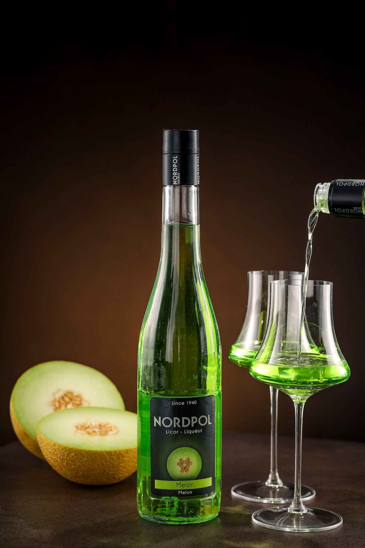 Flasche Nordpol Melón Likör mit frischer Melone und einem eingeschenkten Glas puren Melonenlikörs im Hintergrund.