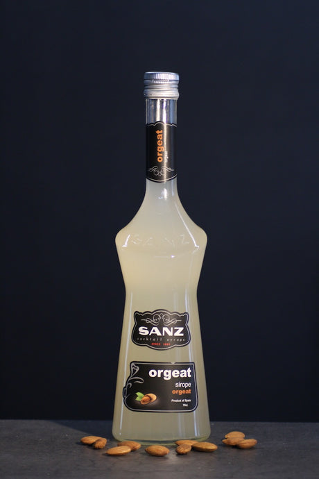 Flasche Sanz Orgeat Sirup, 700 ml, vor schwarzem Hintergrund, umgeben von Mandeln auf einer dunklen Oberfläche.