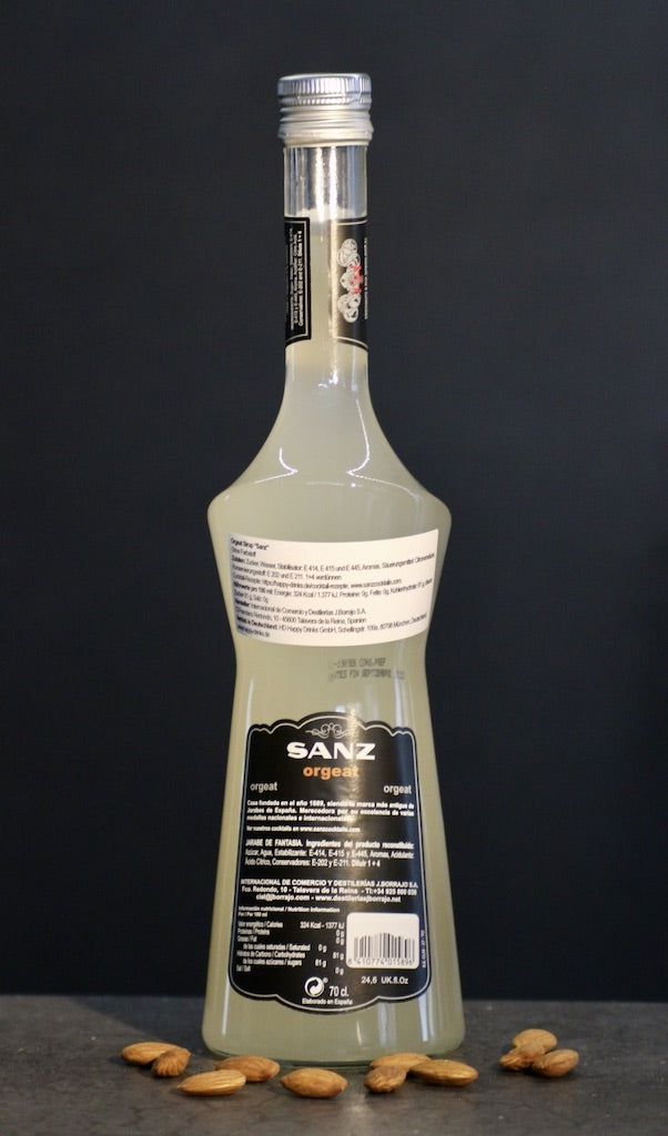 Rückseite der Flasche Sanz Orgeat Sirup, 700 ml, vor schwarzem Hintergrund, mit Mandeln auf einer dunklen Oberfläche.