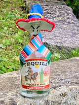 Panchitos Tequila Blanco mit Sombrero auf einem Felsen im Grünen, Flasche mit Kaktusmotiv auf dem Etikett.