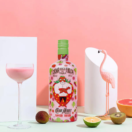 Flasche Capitan Freson Erdbeercreme-Likör mit Tequila, 700 ml, vor rosa Hintergrund, neben Glas, Früchten und Flamingo-Dekoration.