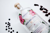 Flasche Samara Gin Hibiskus, Honig & Hagebutte neben Wacholderbeeren und Hibiskusblüten