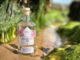 Flasche des Samara Hibiskus, Honig & Hagebutte Gin auf nassem Sand zwischen grünen Felsen, inspiriert von den Tropen Costa Ricas.