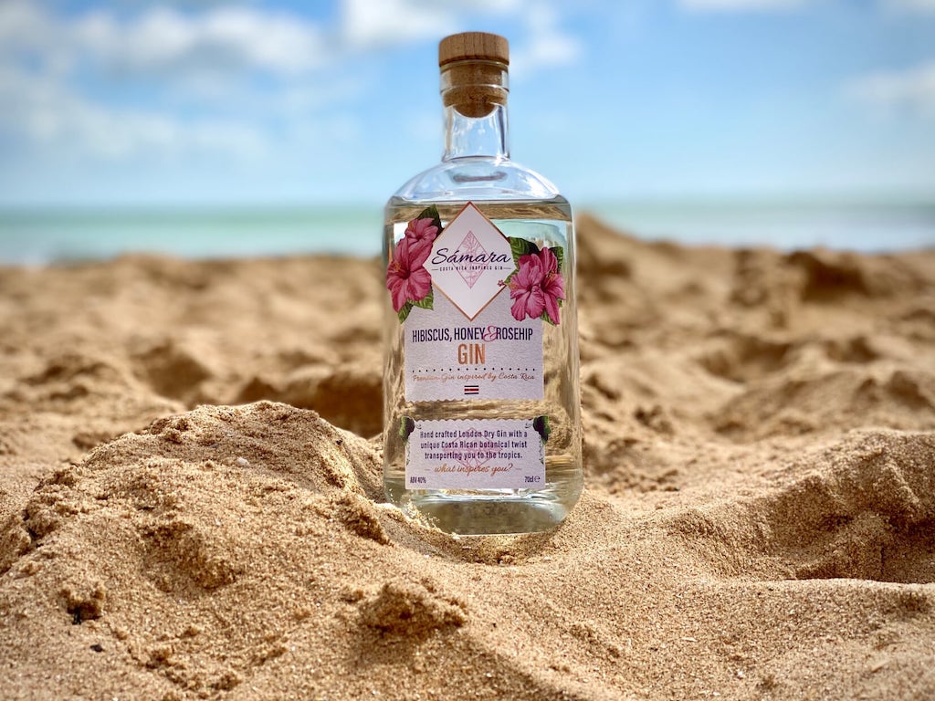 Samara Gin mit Hibiskus, Honig und Hagebutte, inspiriert von Costa Rica, 700 ml Flasche im Sand vor blauem Himmel.