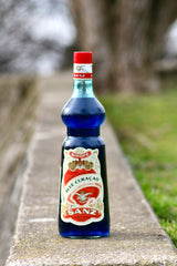 Flasche Sanz Blue Curacao Sirup mit rotem Etikett und Verschluss, 1 Liter, auf einer Steinfläche platziert.