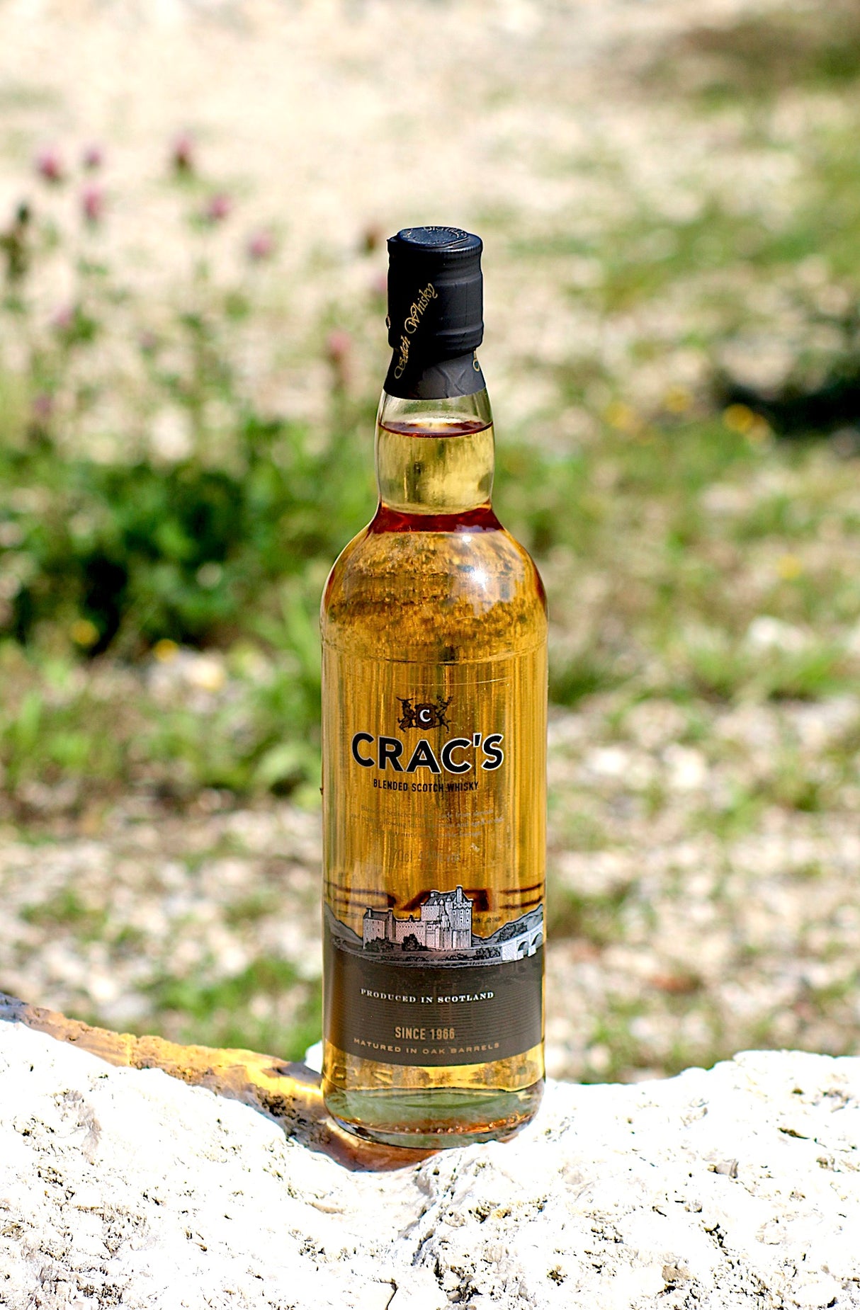 Crac's Blended Scotch Whisky Flasche auf einem Felsen, mit goldenem Whisky und einem Etikett, das ein schottisches Schloss zeigt.