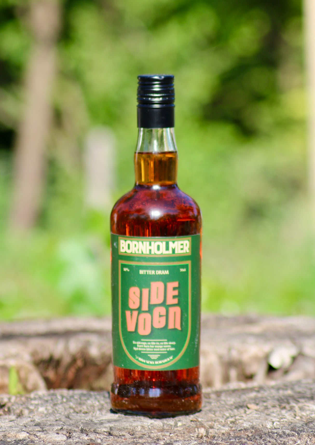 Bornholmer Sidevogn Bitter Dram Flasche auf Baumrinde vor grünem Hintergrund