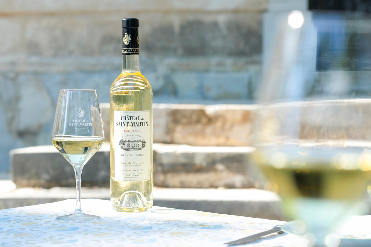 Château de St Martin Grande Réserve Blanc Weißwein mit Glas auf Tisch vor Steinmauer und Treppe