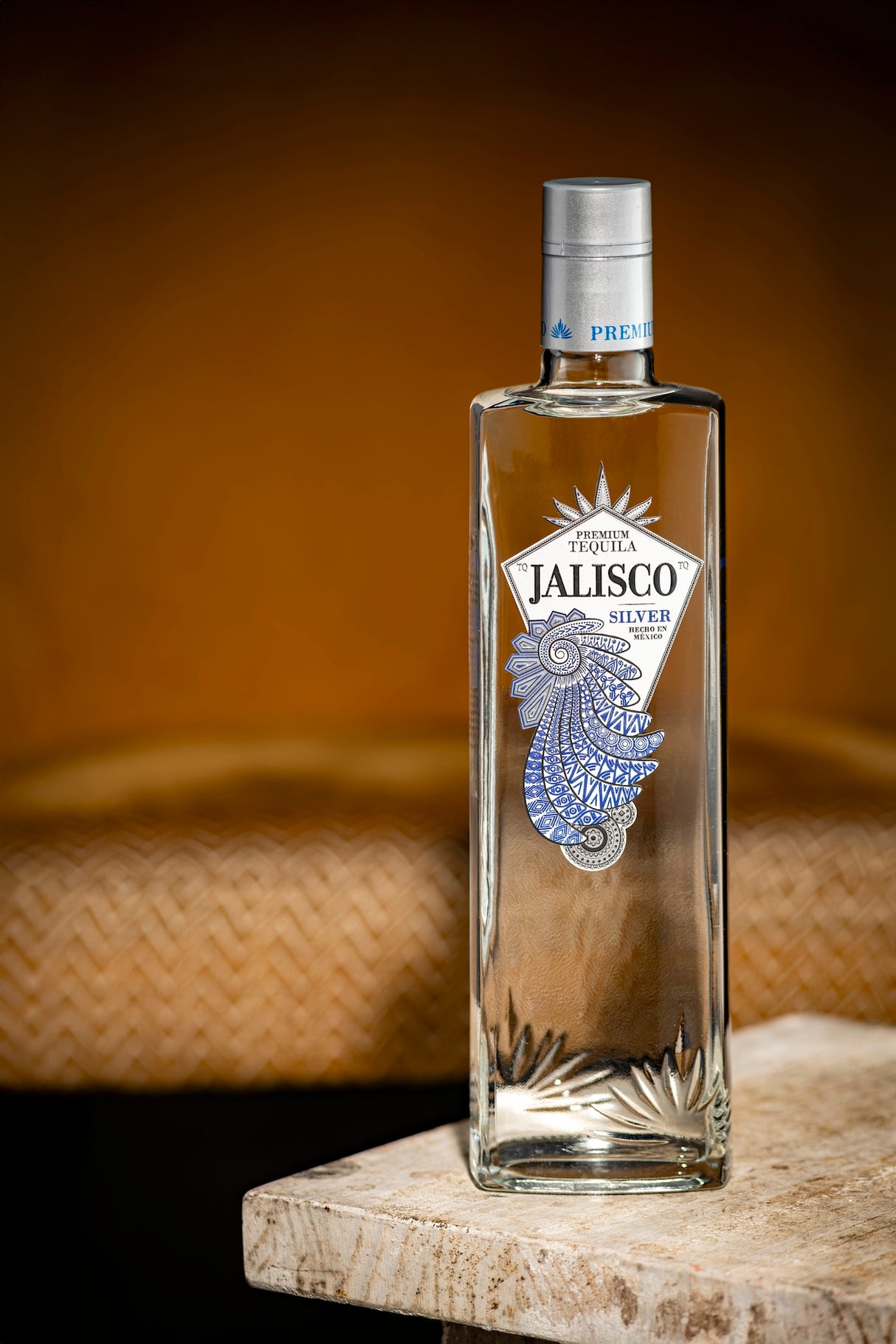 Tequila-Jalisco-Silver-Flasche auf hellem Steintisch vor warmem, unscharfem Hintergrund.