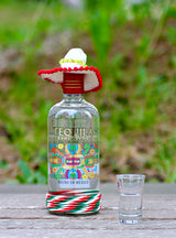 Ranchitos Tequila con Sombrero Flasche mit Shotglas auf Holztisch vor grünem Hintergrund